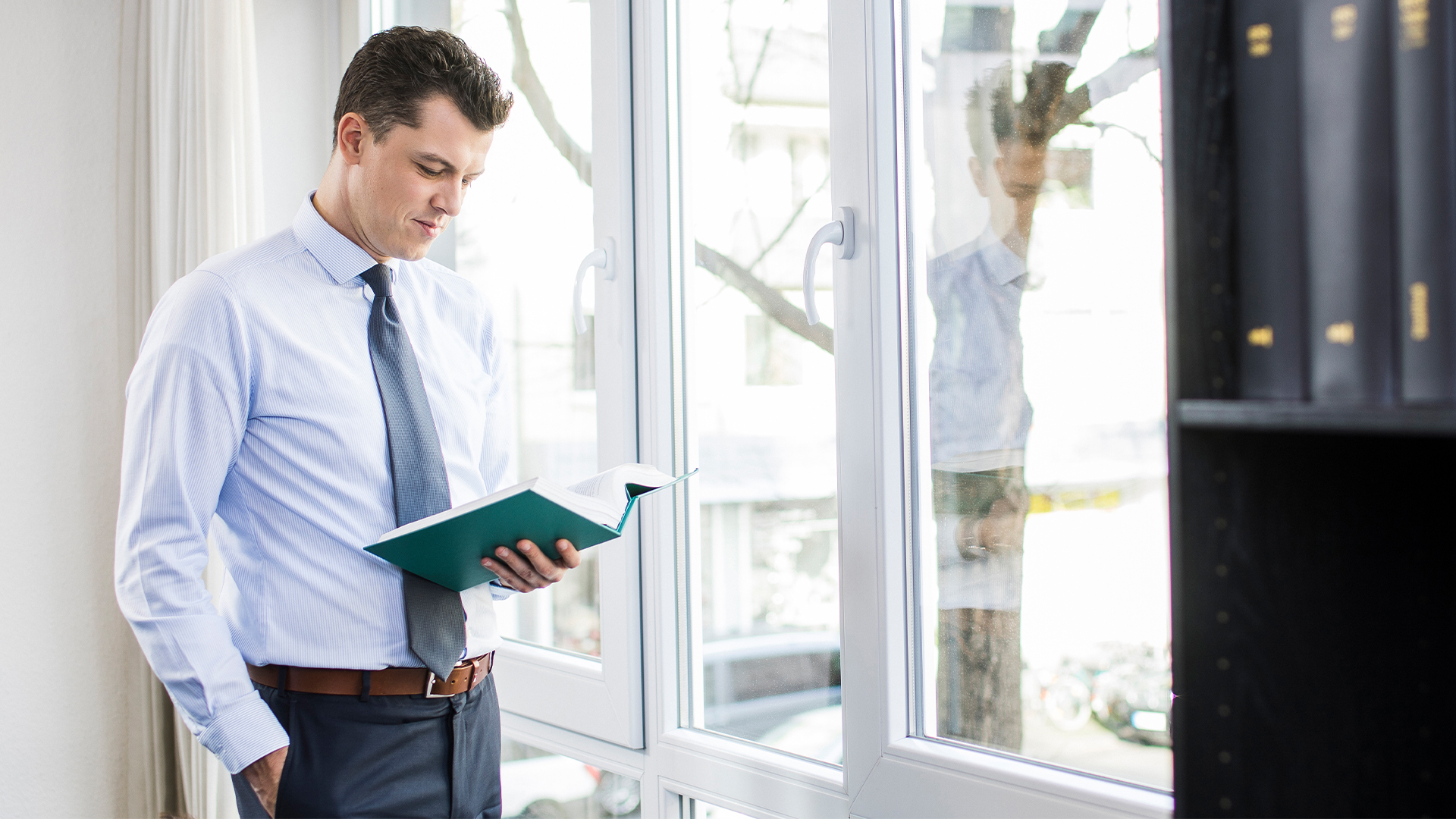 Steuerberater steht am Fenster und liest in einem Gesetzestext